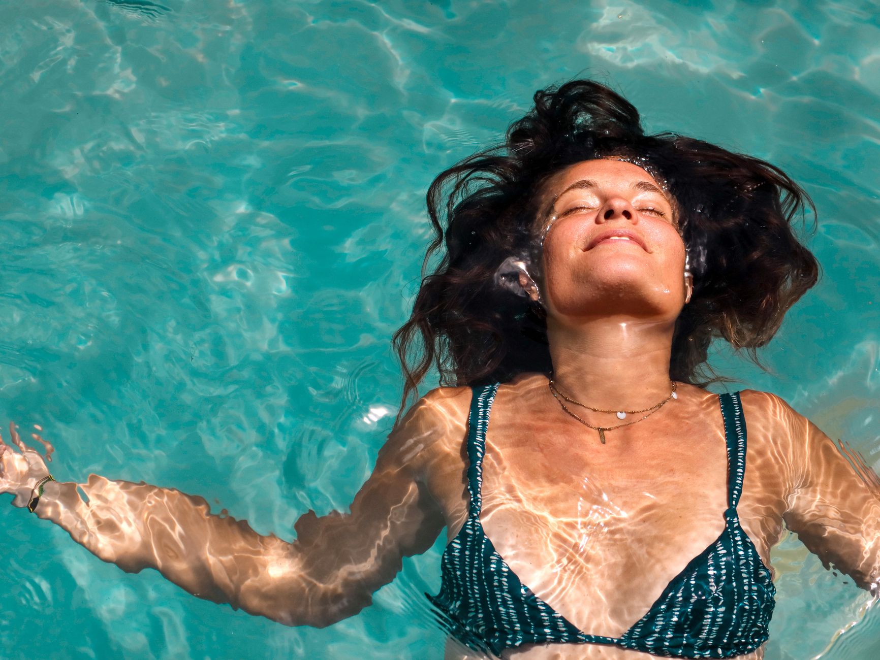 A woman enjoys a peaceful float in a sunlit pool, capturing the essence of summer relaxation.